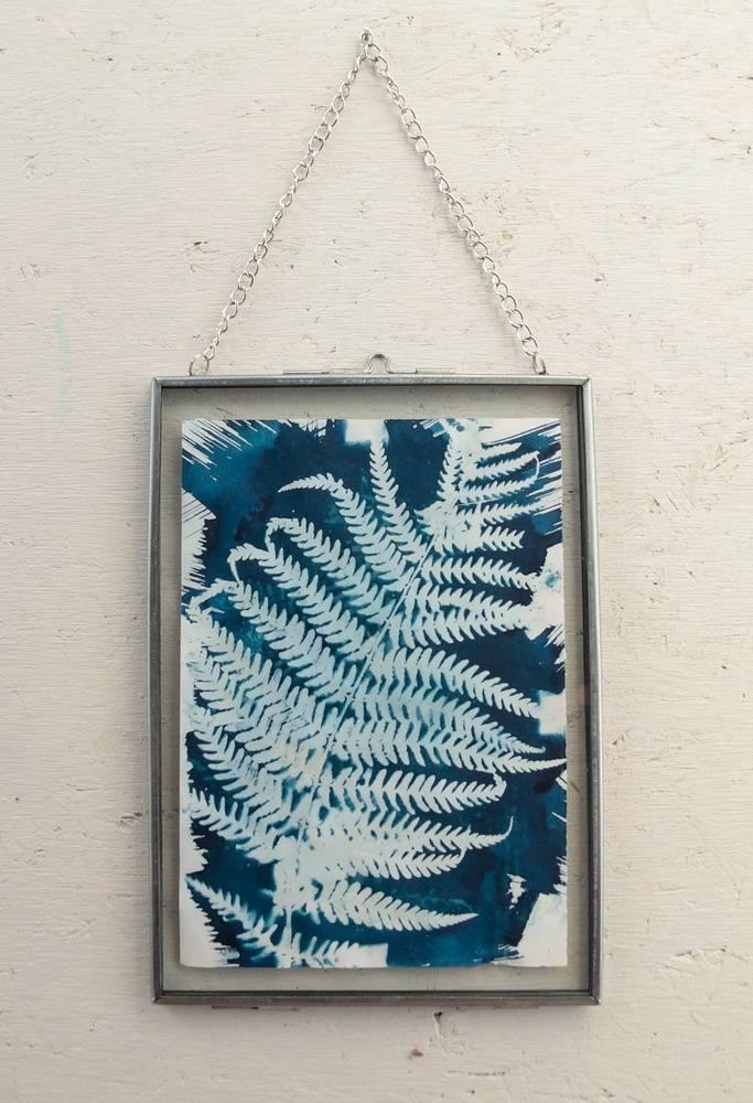 A picture with a gold frame hangs on the wall. It has a blue and white print of a fern leaf.