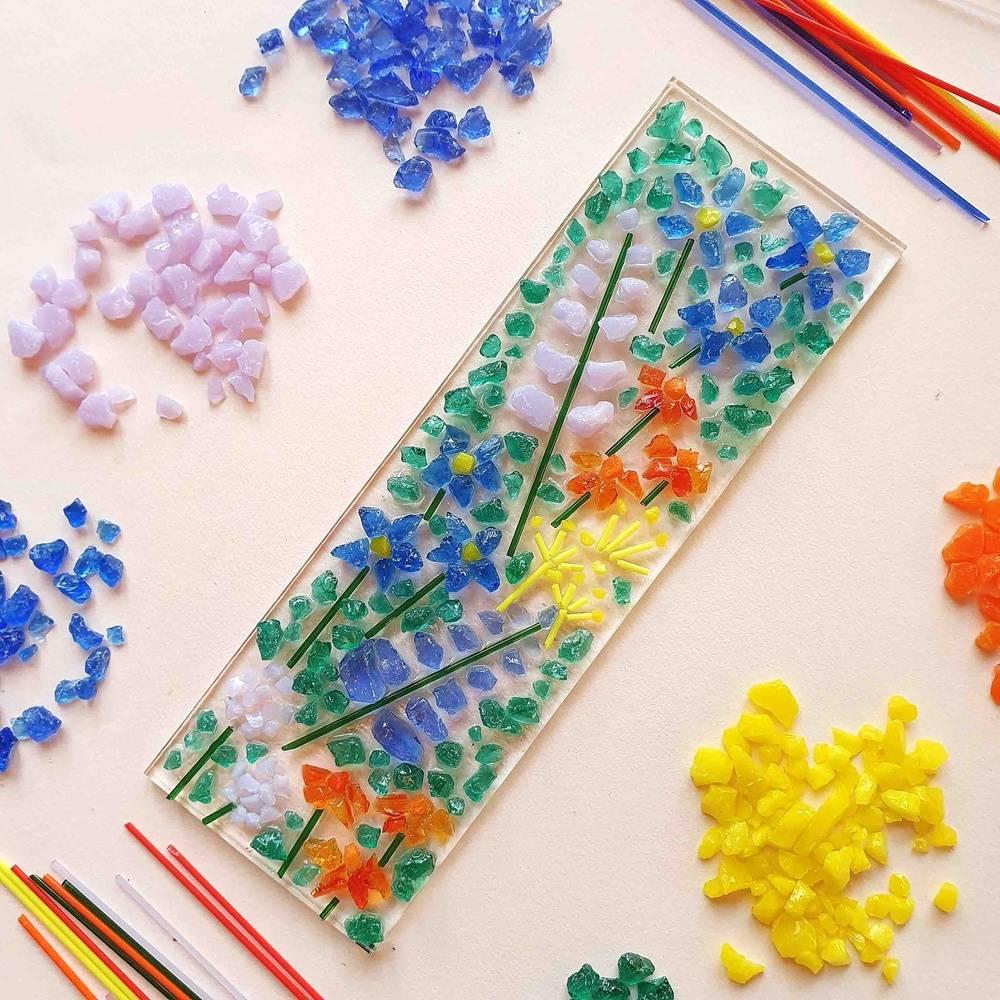 A small, rectangle pane of glass has a colourful picture of flowers, made with tiny pieces of glass