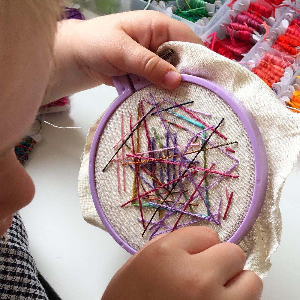 A child holds an embroidery hoop filled with embroiderd, multicoloured straight lines