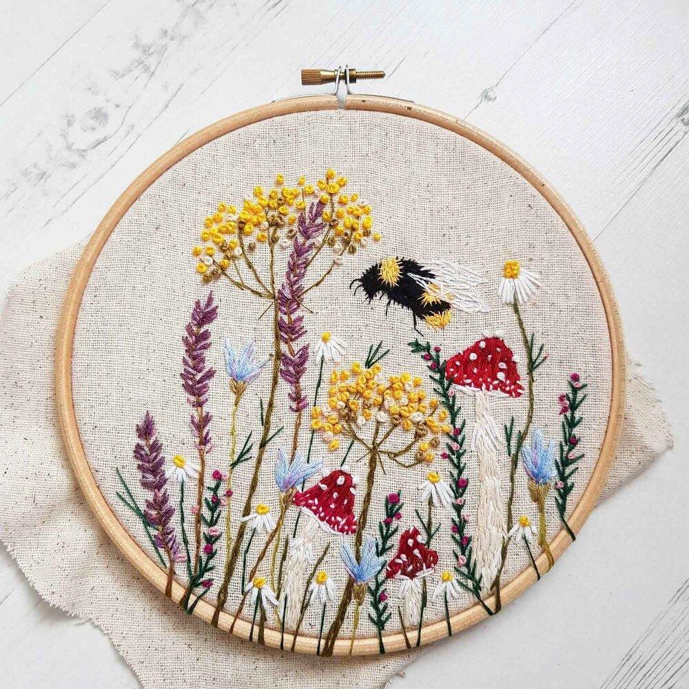 Embroidery hoop with whimsical flowers, mushrooms, and a bumblee.