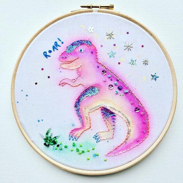 Embroidered purple dinosaur in a whimsical fashion, surrounding by tiny embroidered stars.