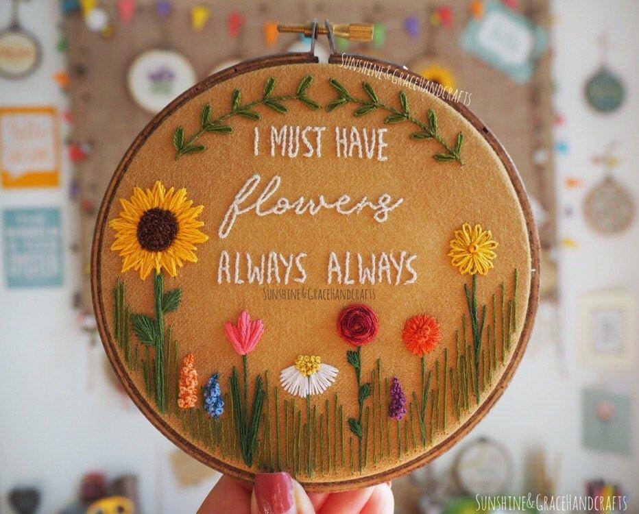 Embroidered flowers on rust coloured fabric. The quote in the middle reads: "I must have flowers always, always".